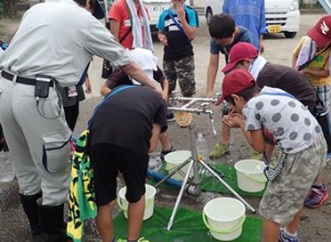 訓練で開設した災害時給水栓から水を飲む子供たちのようす